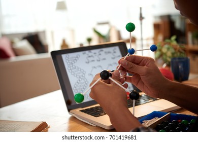 Hands of student assembling molecular model according to directions on laptop screen