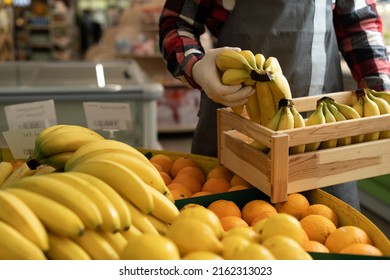 Hands Of A Supermarket Seller Worker In An Apron Arranging Citrus Fruits And Bananas In The Fruit Section, Close-up