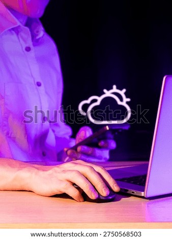 Hands at table with computer and phone featuring illuminated cloud icon in neon purple setting.