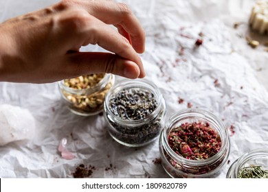 Hands take a pinch of spice from a glass jar. Dried flowers, lavender and rosemary