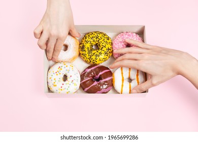 Hands is taking colored glazed donuts in donut box. Hands is grabbing different flavors doughnuts. Unhealthy snack in the office or a break office. Copy space, mock up - Powered by Shutterstock