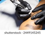 Hands of tattoo artist in black gloves busy with work at tattoo shop. 