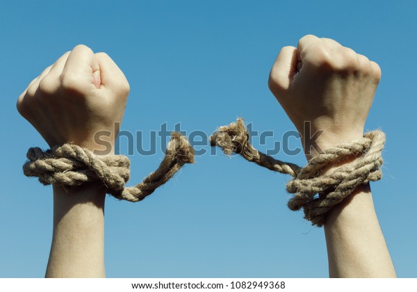 Hands tearing shackles the background of blue\
sky. Concept of freedom