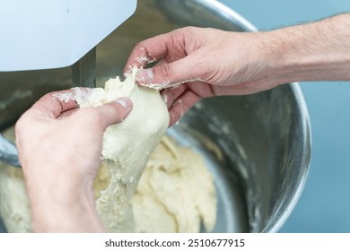 The hands of a technologist or baker check the readiness and quality of the dough in a production or planetary mixer. High quality photo - Powered by Shutterstock