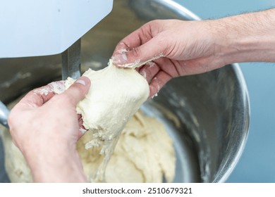 The hands of the technologist or baker check the readiness and quality of the dough in the production or planetary mixer. High quality photo - Powered by Shutterstock