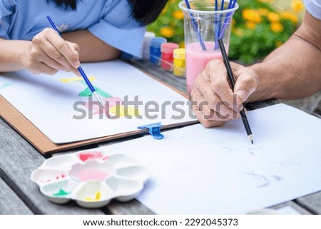 hands of teen girl painting watercolors and grandfather drawing on paper, grandfather and granddaughter spend leisure time doing artwork,drawing work together