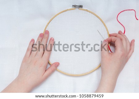 Hands of teenage girl with needle on embroidery frame on white textile background canveplian top view flat lay 