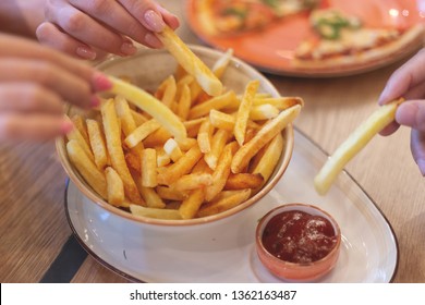 Hands Of Three Young People Sharing Bowl Of French Fries And Dipping Them Into Ketchup Before Eating In Restaurant