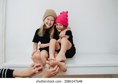 Hands tickling feet of cute boy and girl sibligs. They are wearing in colorful knitted hats, sitting on a table.