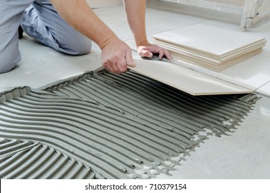 The hands of the tiler are laying  the ceramic tile on the floor. - Shutterstock ID 710379154