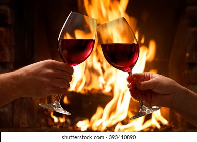 Hands toasting wine glasses in front of lit fireplace - Powered by Shutterstock