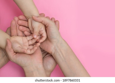 hands together the family on a pink background, copy space, parents holding the hands of a kid along - Shutterstock ID 1897860331