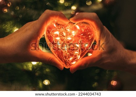 hands together forming a heart of red led lights and a background with diffused lights.