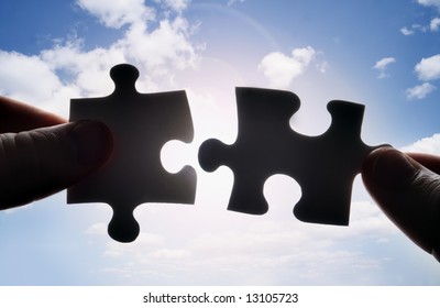 Hands Trying To Fit Two Puzzle Pieces Together