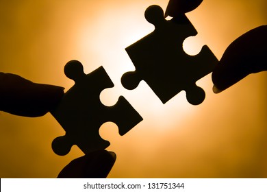 Hands Trying To Fit Two Puzzle Pieces Together.