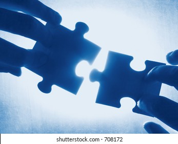 Hands Trying To Fit Two Puzzle Pieces Together