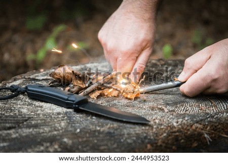 Hands trying to start a fire with a magnesium steel in the woods using bushcraft tools