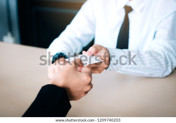 Hands of two business people sitting\
in office room giving and taking empty business\
card.