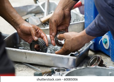 Hands Of Two Car Mechanics Cleaning Gearbox Parts In Petrol.