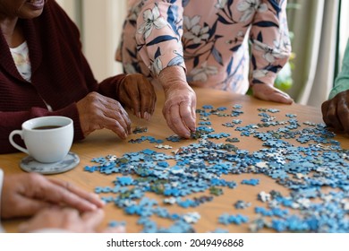 Hands of two diverse senior women and african american male friend doing puzzles. socialising with friends at home. - Powered by Shutterstock