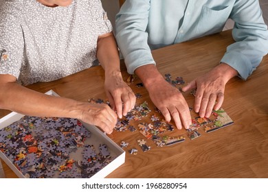 Hands of two elderly people at home  playing with jigsaw puzzle on wooden table