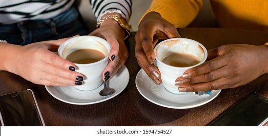 Hands of two multi ethnic girl friends enjoying coffee together in a coffee shop. Close up of hands holding coffee cups. - Powered by Shutterstock