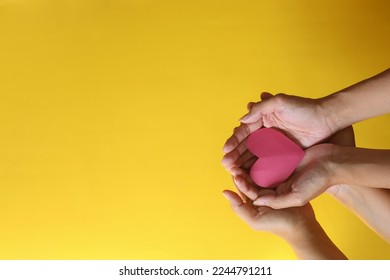 Hands of two people holding a red heart shape on yellow background with copy space.  - Shutterstock ID 2244791211