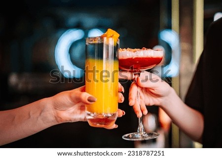 hands of two unknown women holding and clinking glasses cocktails in restaurant