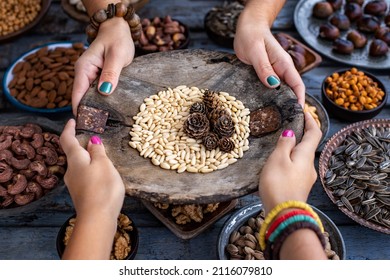 Hands of two women holding a wood bowl of pine nuts. Pinenut concept with other nuts. 