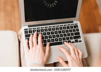 Hands typing on laptop while waiting for application to load in cozy indoor setting