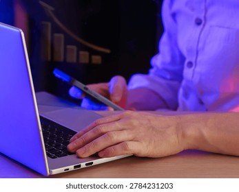 Hands typing on laptop while holding phone, upward bar chart displayed in illuminated background