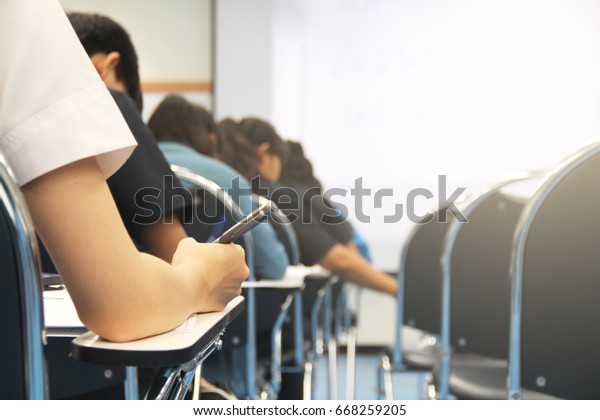 Hands university student holding pen writing\
/calculator doing examination / study or quiz, test from teacher or\
in large lecture room, students in uniform attending exam classroom\
educational school.