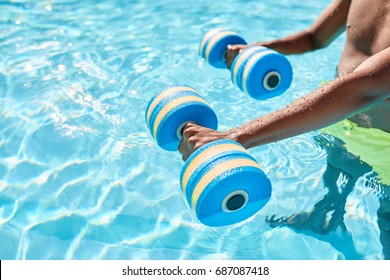 Hands Of An Unknown Black Guy Holding Dumbbells For Aqua Aerobics Standing In The Swimming Pool On Warm Summer Day