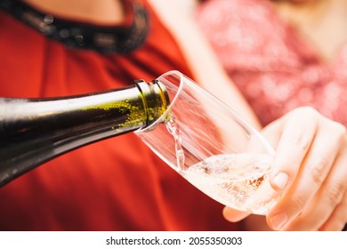 The hands of an unknown woman wearing a red dress holding a glass as she fills it with cava from a green glass bottle. - Shutterstock ID 2055350303