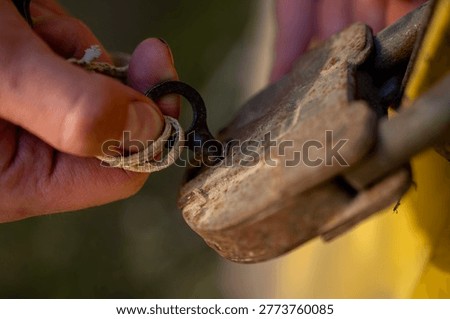 Hands unlocking a rusty padlock with a key on a yellow metal door, showing manual access to a locked entrance outdoors.