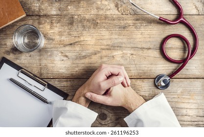 Hands of unrecognizable doctor laid on a table. Wooden desk background.