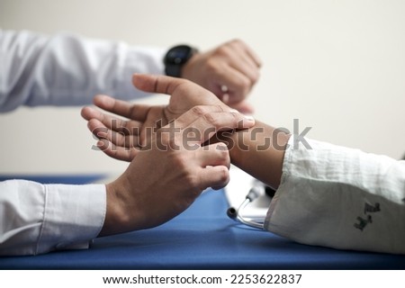 hands of unrecognizable doctor looking at his watch and feeling radial pulse of patient