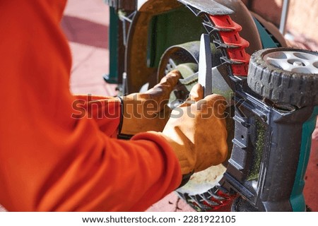 Hands of an unrecognizable gardener holding a file to sharpen mower blades. Backyard lawn maintenance concept.
