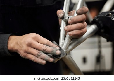 Hands of an unrecognizable hispanic man sanding an unpainted bicycle frame as part of the process of a bike renovation work made at his workshop. - Shutterstock ID 2365682245