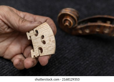 Hands of an unrecognizable Latin American luthier holding a violin bridge, in the background a violin head. Concept of stringed instruments