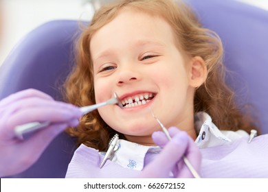 Hands of unrecognizable pediatric dentist making examination procedure for smiling cute little girl sitting on chair in hospital. Dentist office. Little girl sitting in the dentists office - Powered by Shutterstock