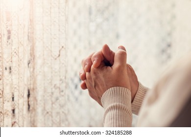 Hands of an unrecognizable woman standing by the window and praying