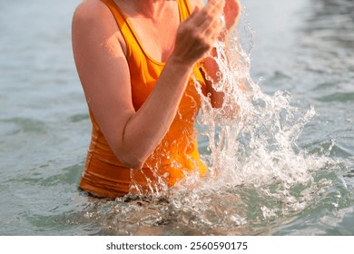 The hands of an unrecognizable woman in a yellow T-shirt splash sea water. - Powered by Shutterstock