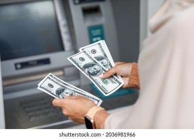 Hands Of Unrecognizable Young Arabian Business Woman In Hijab Counts Dollars Near Atm With Empty Screen, Cropped. Online Payment, Money Transfers, Financial Transactions And Digital Financial Services