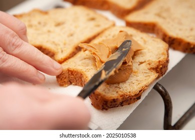 Hands using a black plastic knife to spread peanut butter on wheat bread