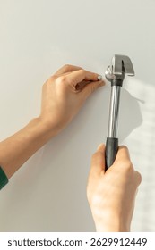 Hands using a hammer to drive a nail into the wall in a bright and airy indoor space during daylight