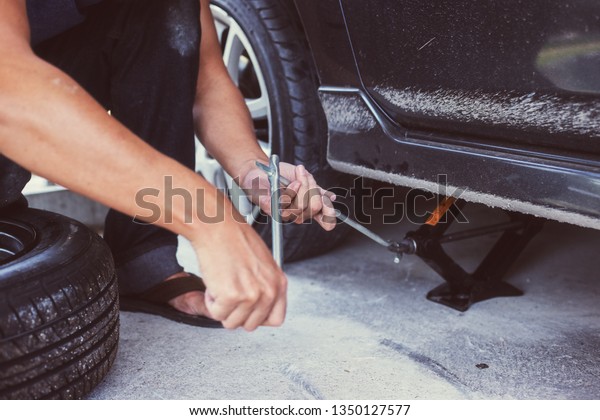 Hands using hydraulic jack -\
car maintenance concept. Car tire changed for maintenance in garage\

