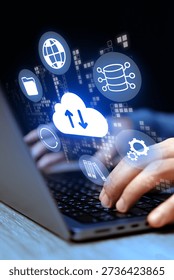Hands using a laptop with cloud computing icons in a dark setting