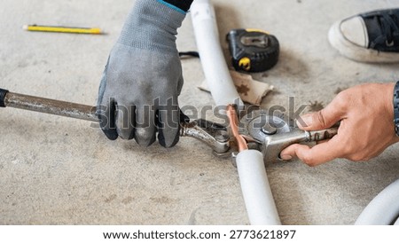 Hands using manual pipe bender tool to bend copper tube for air conditioning installation, HVAC technician in gloves using a manual lever tube bender for copper piping work in refrigeration system