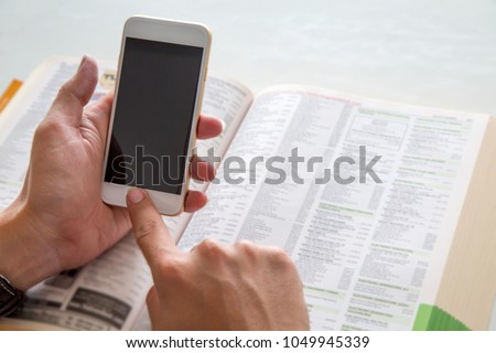 Hands using mobile phone for calling to the service shop in directory book.